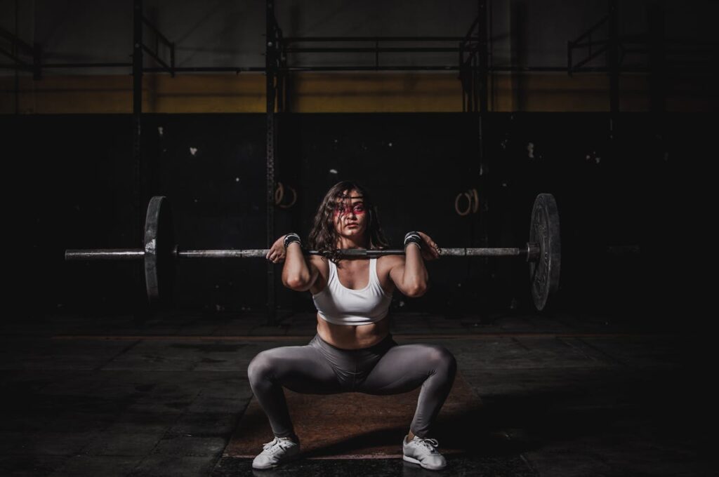 Mastering the First Impression: Your intriguing post title goes here A strong female weightlifter squats with a barbell in a dimly lit gym, showcasing power and fitness.